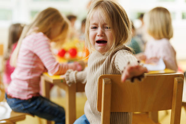 Little girl crying in kindergarten while sitting at the table whit her friends