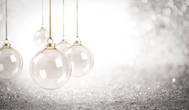 White Christmas baubles hanging from a gold string against a sparkling white background. The scene is minimalist yet elegant, highlighting the glossy surface of the ornaments and the bright, festive atmosphere.