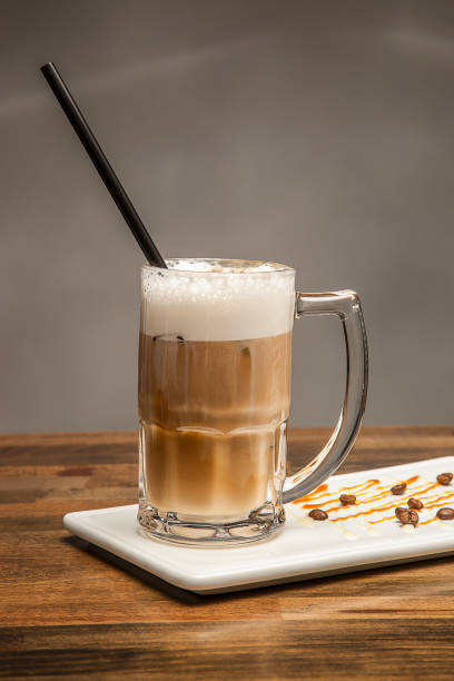 iced Caramel Cafe Latte topped with whipped cream and a drizzle of caramel sauce served in jar isolated on wooden table side view of cafe dessert drink