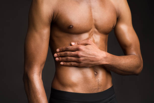 Unrecognizable black man showing body on dark wall Bodybuilding Concept. Strong athletic afro man with muscular naked torso touching his body over black studio wall man muscular chest stock pictures, royalty-free photos & images