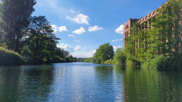istock Scenic river view with lush greenery and old building under blue sky. 2175966488
