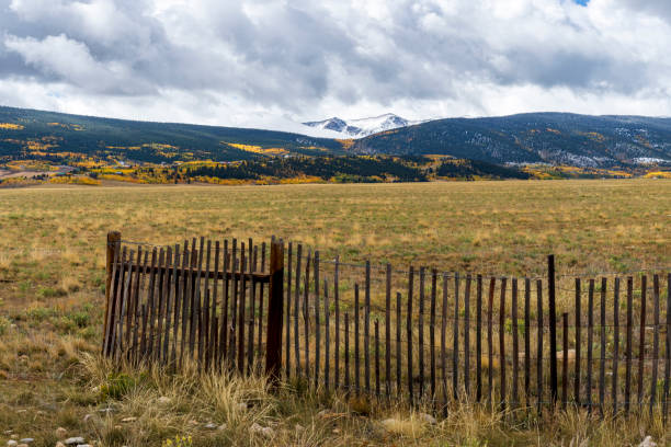 A scenic view of a wooden fence in a lush green field with mountains and a clear blue sky in the background.