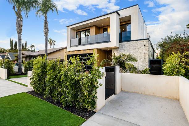 Modern two-story house with lush greenery and palm trees. Modern two-story house with a clean and minimalist design, featuring a front yard with lush greenery and palm trees under a blue sky. two-story-house stock pictures, royalty-free photos & images