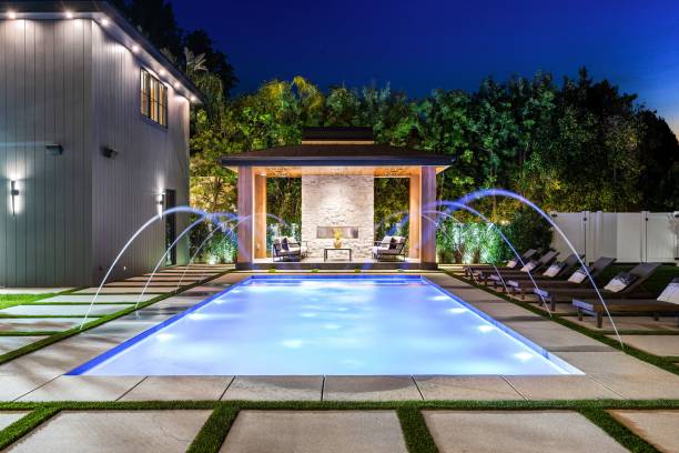 Luxurious modern backyard with illuminated swimming pool, lounge chairs, and a covered seating area at night.