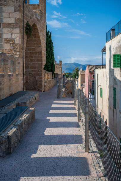 A scenic walkway along a historic stone building with a mountain view and clear blue sky, located in Alcudia, Mallorca