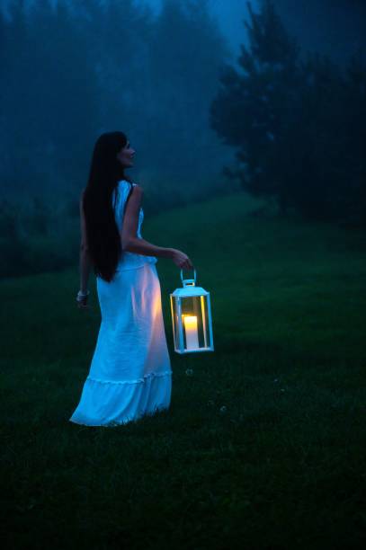 istock Woman with lantern in misty forest at dusk 2175977646