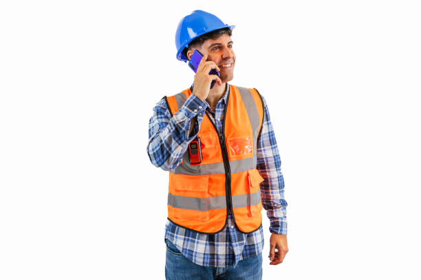 engineer in an orange safety vest and hard hat is on a phone call using a smartphone at a construction site. The scene captures the multitasking nature of the job white background
