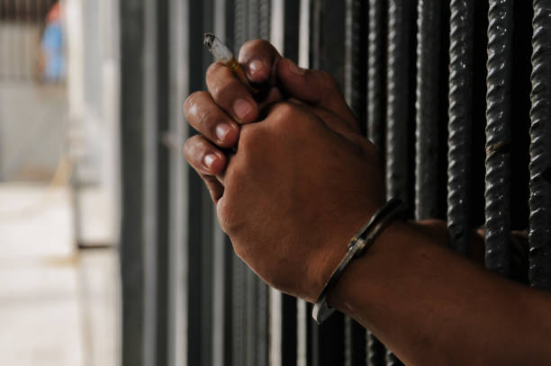 istock hands of a prisoner behind prison bars on black background 2175994869