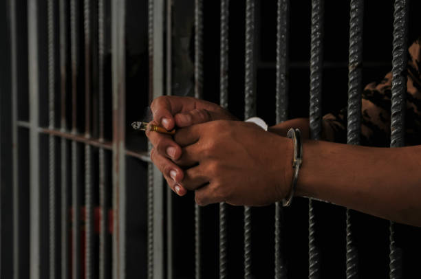 istock hands of a prisoner behind prison bars on black background 2175994895