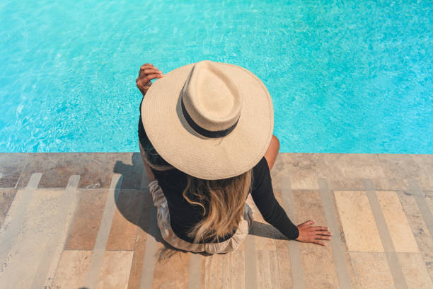 istock A woman wearing a straw hat sits on a stone staircase by a pool 2175995302