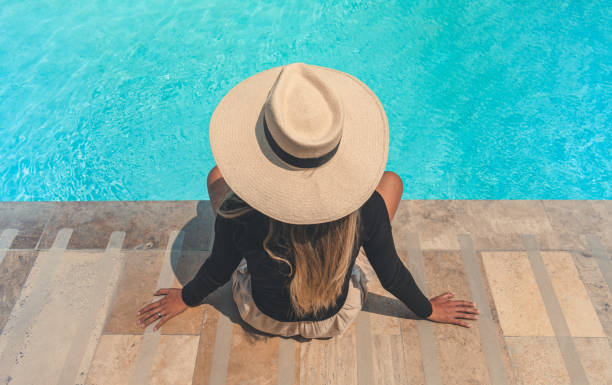 istock A woman wearing a straw hat sits on a stone staircase by a pool 2175995401
