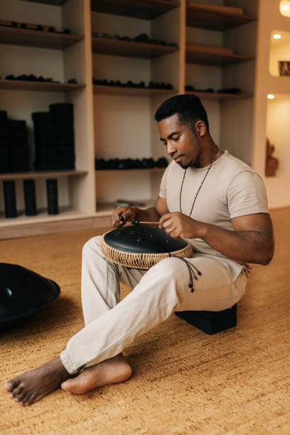 istock Peaceful African man in trance playing meditative instrument tank drum using drumsticks sitting on floor in meditation room. Silence calm filling room by sounds 2176001018