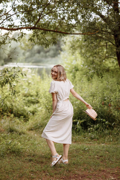 istock Woman standing in park holding straw hat. 2176043509
