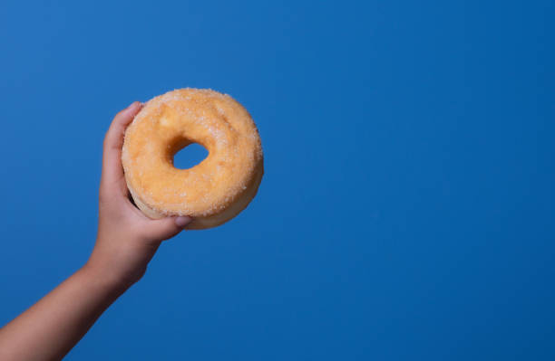 istock Child's hand holding donut against blue background 2176049397