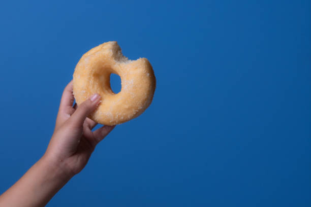 istock Child's hand holding donut against blue background 2176049399