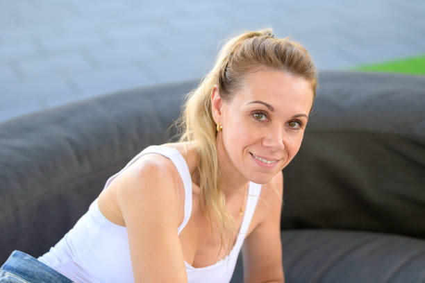 Young blonde woman languidly leaning on her soft couch, in a white living room. Perfect teeth, dreaming or inventing. Her mind is focused on a profitable plan, making the most of her education