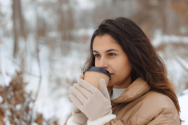 istock Young cute swarthy brunette woman drinking coffee from papper cup in snowy winter forest 2176064372