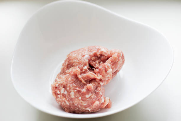 High angle view of raw meatballs shot on rustic wooden kitchen table. Some cooking and seasoning ingredients like rosemary, garlic, peppercorns, olive oil and oregano are on the table. Predominant colors are red and brown. Low key DSRL studio photo taken with Canon EOS 5D Mk II and Canon EF 70-200mm f/2.8L IS II USM Telephoto Zoom Lens