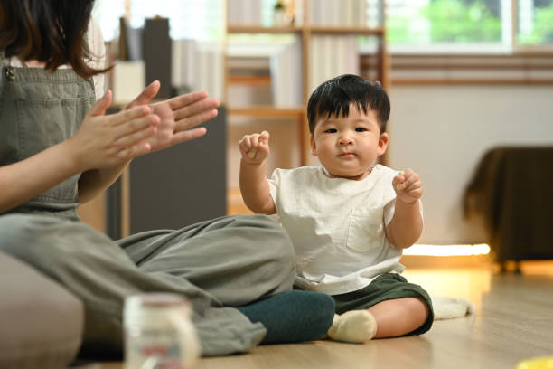 Happy mother playing with cute little baby boy on a wooden floor at home. Child care concept stock photo