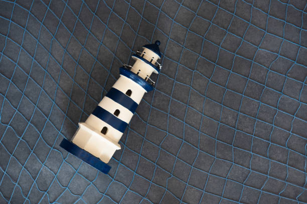 Handmade crochet lighthouse on blue background with felt clouds. Minimalist nautical-themed flat lay with soft textures and vibrant colors, top view