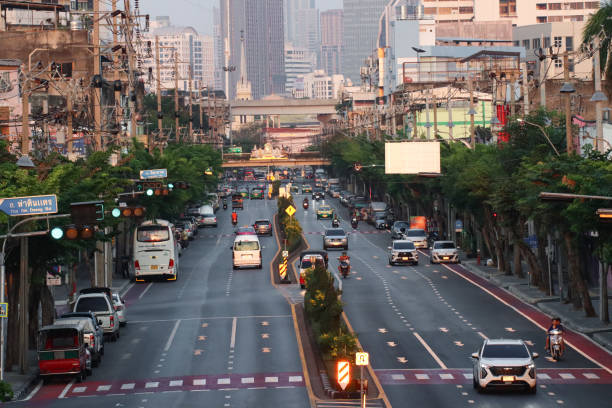 Bangkok, Thailand - February, 18 2024: Stock photo showing  view from overpass of elevated SkyTrain line traversing traffic with motorcycles, cars and taxis seen driving on multilane Sukhumvit Road, Bangkok, Thailand.