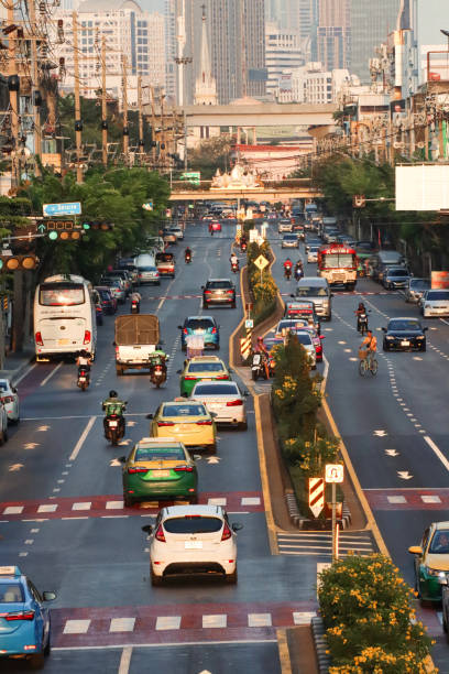 Bangkok, Thailand - February, 18 2024: Stock photo showing  view from overpass of elevated SkyTrain line traversing traffic with motorcycles, cars and taxis seen driving on multilane Sukhumvit Road, Bangkok, Thailand.