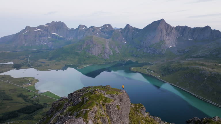 AERIAL: Man walking on a peak, in front of the sea and Lofoten mountains, Norway