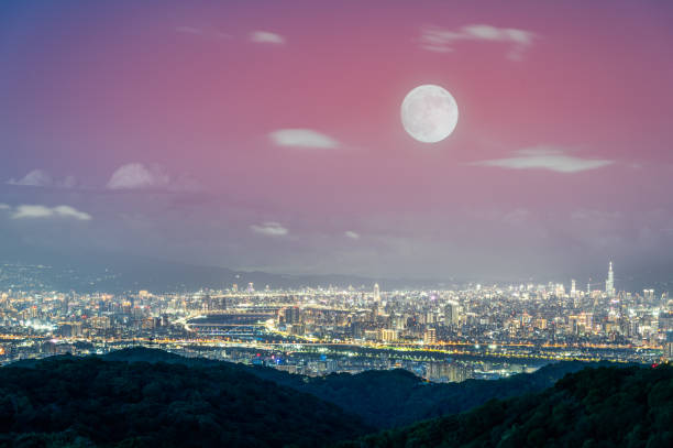 A golden autumn moon hangs over the Taipei skyline, casting a warm glow on the city. The scene captures the tranquility of an autumn evening. Taipei City, Taiwan.