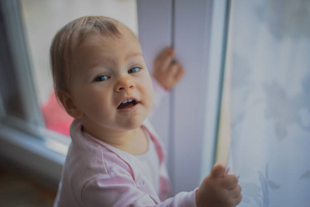 A small baby is playing by the window