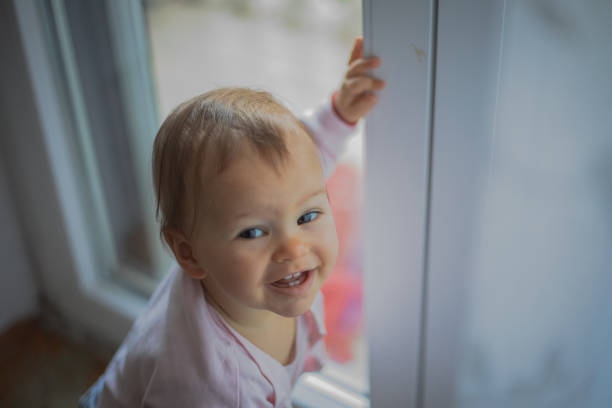 A small baby is playing by the window