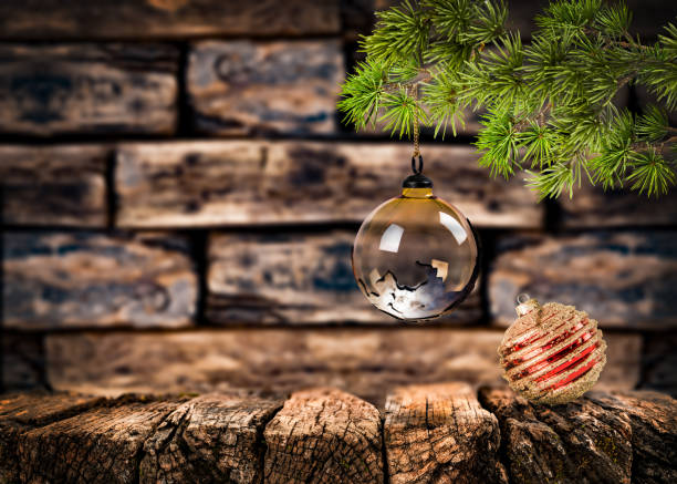 A Glass Christmas ornament hanging from a pine branch, set against a rustic, blurred wooden background