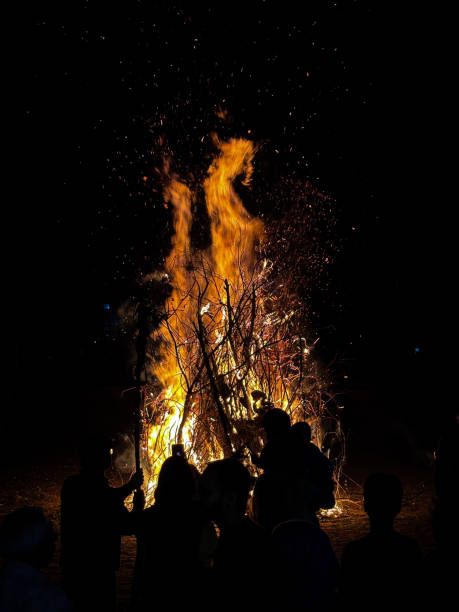 istock Image of silhouetted figures backlit by roaring bonfire, sparks flying in dark night sky, crowds celebrating Guy Fawkes bonfire night 2176135102