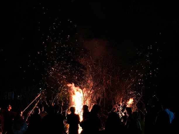 Stock photo showing silhouetted outlines of crowd of people backlit by a bonfire at nighttime. These unrecognisable spectators are watching roaring flames and sparks dancing in the dark, night sky.* Not AI modified *