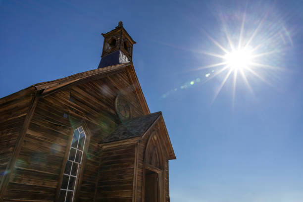Sunburst shines over an old wooden church in Bodie State Historical Park, a preserved ghost town from the Gold Rush era in California, USA, offering a glimpse into the Old West.