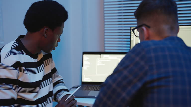 Multiracial software developers engaged in a discussion on code and software development in a high-tech office at night. Coding, computer languages, and data science are highlighted in this collaborative environment. Focus on cloud computing.