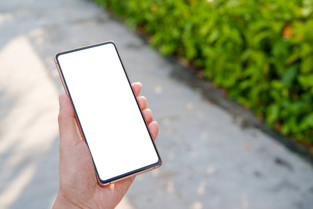 istock A high-angle view shows a hand holding a mobile smartphone with a blank screen, set against the blurred backdrop of a walkway in an outdoor park. 2176154039
