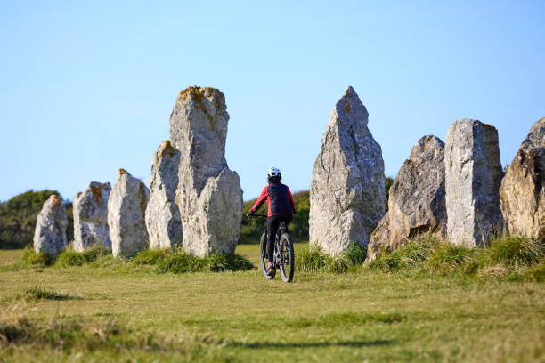 woman cycling between the neolithic menhirs of Camaret sur mer in Brittany, France