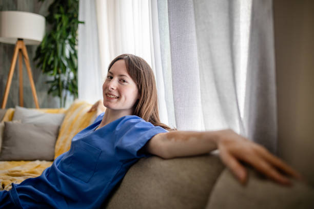 istock Woman in blue scrubs smiling on a cozy beige sofa 2176173192