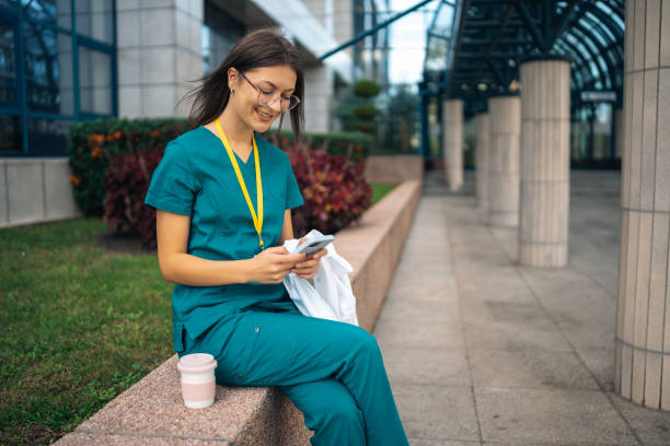 istock Nurse sitting on bench, texting on phone outdoors. 2176180425
