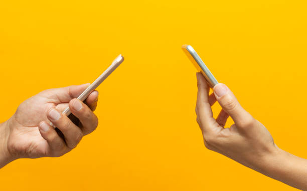 istock Two Hands Holding Smartphones Facing Each Other on a Yellow Background 2176185450