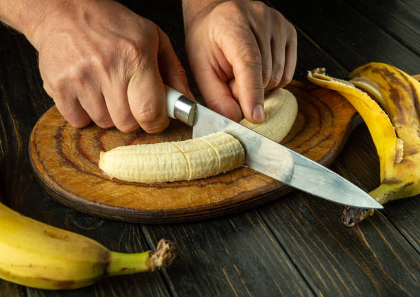 istock Hands of a cook using a knife on a kitchen board cutting a ripe banana for a diet menu or dish. Bananas diet concept 2176185532