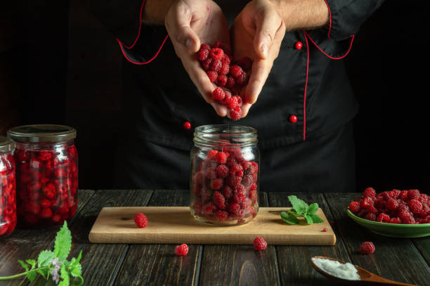 istock The cook prepares jam with Rubus idaeus. The concept of making sweet raspberry jam on the kitchen table. Filling the jar with ripe berries in the hands of the chef 2176185540