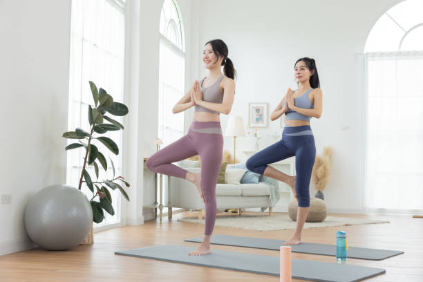 木のポーズをとる2人の女性 アサナヨガ またはヴルクササナ リビングルームでポーズ - ヨガ ストックフォトと画像