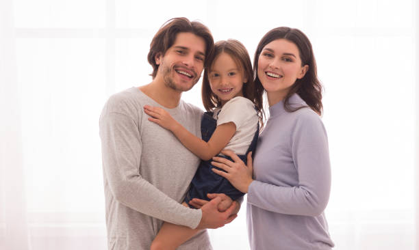 istock Smiling Parents Holding Little Daugher In Arms And Posing At Camera 2176199071