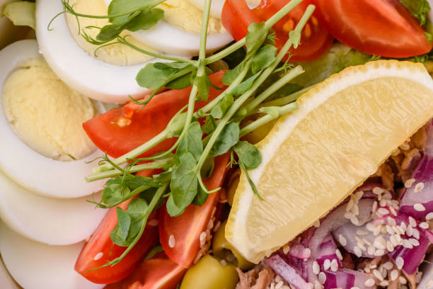 Salad with tuna pieces, boiled egg, cherry tomatoes, lettuce, salt, spices and microgreens