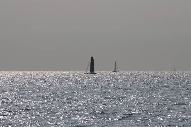 Sailing boats gliding along the gently rolling surface of turquoise blue sea. Favorable sailing conditions and a beautiful sunny summer day to explore the picturesque English coastline from a boat.