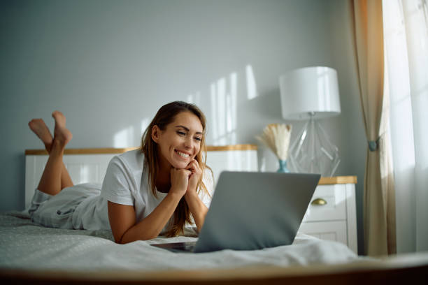 istock Young happy woman using laptop while relaxing in bedroom. 2176214886