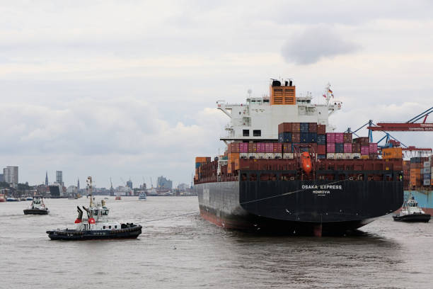 Hamburg, Germany - 09 16 2024: Osaka Express Monrovia container ship from behind with tugs in the harbor