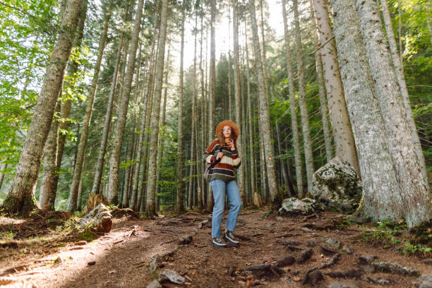 istock A young woman stands in a sunlit forest, surrounded by tall trees. 2176226347