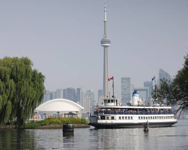 Toronto, Canada - August 27, 2024: Hundreds of passengers on the Thomas Rennie ferry arrive at the Toronto Islands on a summer morning. The downtown skyline with the Rogers Centre and CN Tower are in the background.